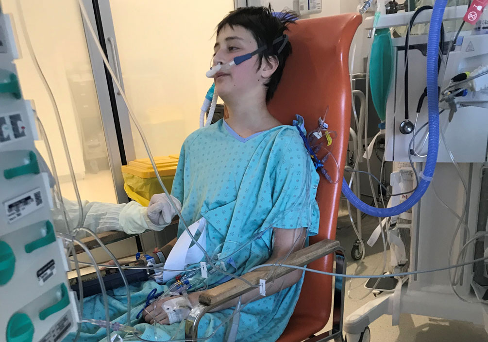 Olivier Lanthier est assis sur une chaise en blouse d'hôpital, entouré de matériel médical.