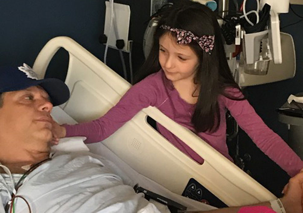 Paul couché dans un lit d'hôpital avec sa fille à ses côtés