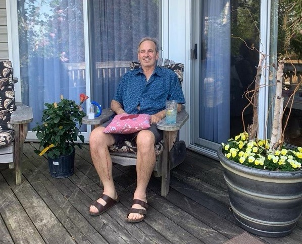 Paul King est assis sur une chaise à l’extérieur, un oreiller sur les genoux.