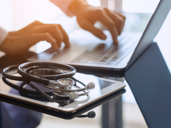 Un ordinateur portable, une tablette et un stéthoscope posés sur une table